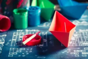 Colorful paper boats on a blackboard.