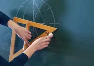 A woman is holding a triangle on a blackboard.