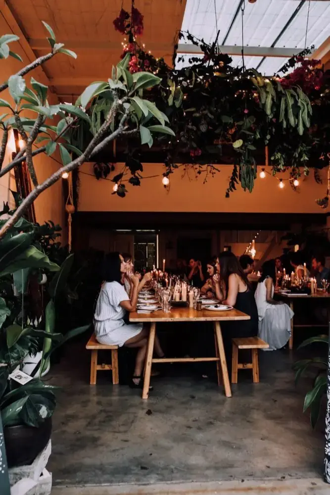 Unrecognizable people having banquet at tables in restaurant near plants