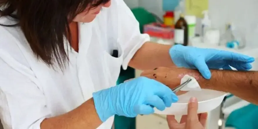 A healthcare professional cleans a wound using medical instruments,