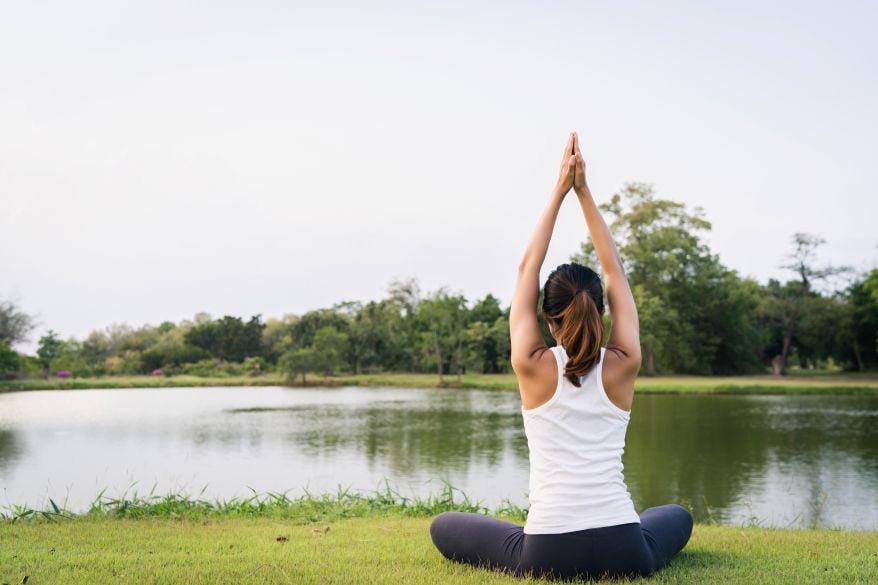 Woman meditating by a lake, connecting with nature for better health.